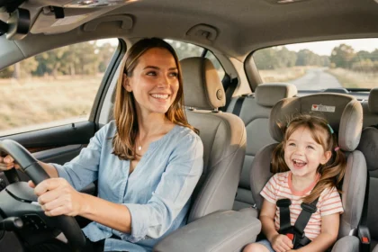 Mère souriante conduisant avec sa petite fille de 4 ans qui rit sur la banquette arrière pendant un trajet en voiture